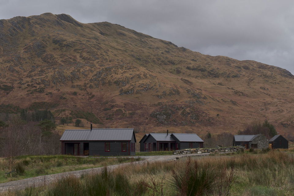Dark timber cottages with gabled metal roofs at the foot of a Highland mountain on Kilchoan Estate.