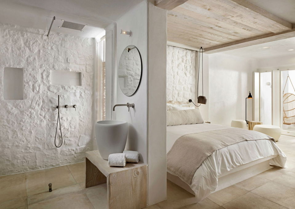 A modern bedroom and bathroom area with white textured walls, a light wood ceiling, and light-colored furnishings.