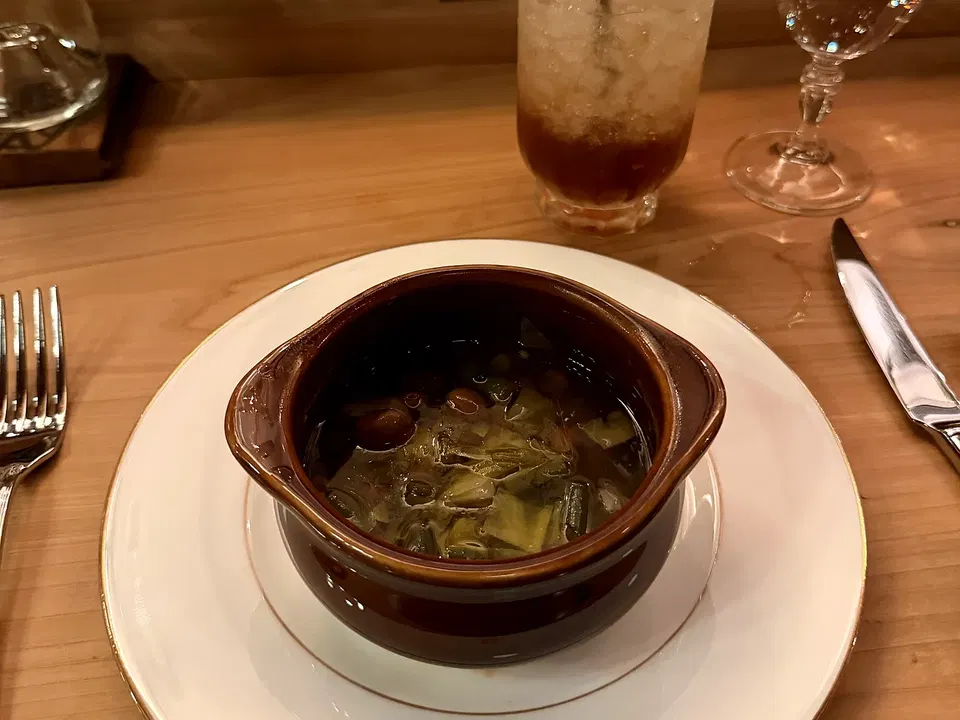 A ceramic bowl of garbure served at La Cigale with greens visible in the broth