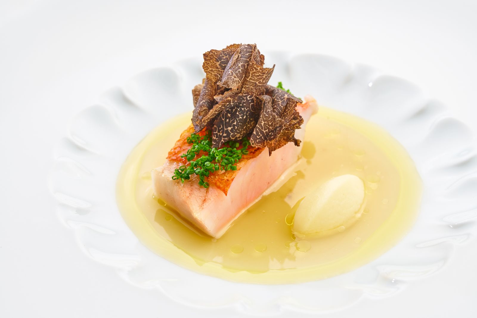 A fine-dining plated dish featuring monkfish with truffle shavings, chives, and a yellow sauce, published by Condé Nast Traveler in an article explici
