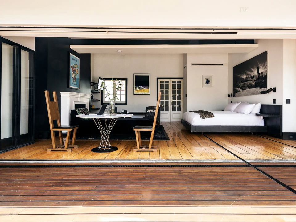 A modern hotel bedroom suite with black-framed folding glass doors, hardwood floors, contemporary furniture, and a black accent wall