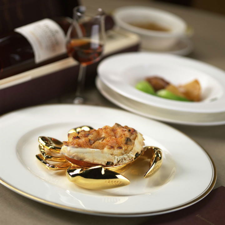 Fine-dining dim sum presentation on a gold crab-shaped dish holder, served on white china with gold rim; the source page explicitly names T'ang Court 