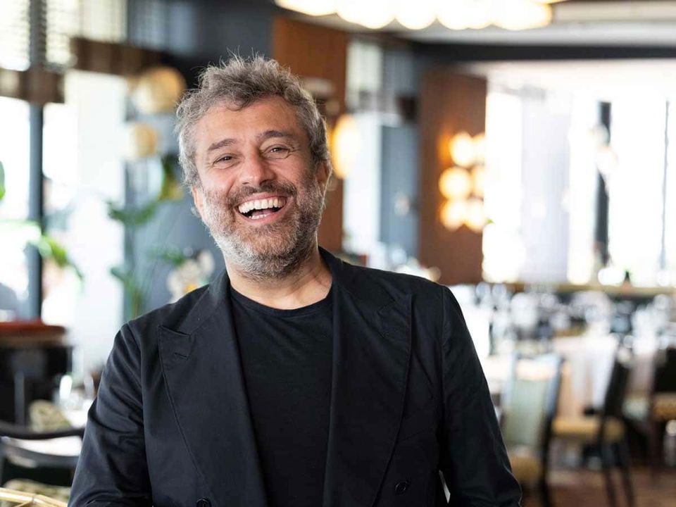 Portrait of a middle-aged man with gray hair and beard, smiling broadly in a restaurant setting; the source page (Gambero Rosso International) explici
