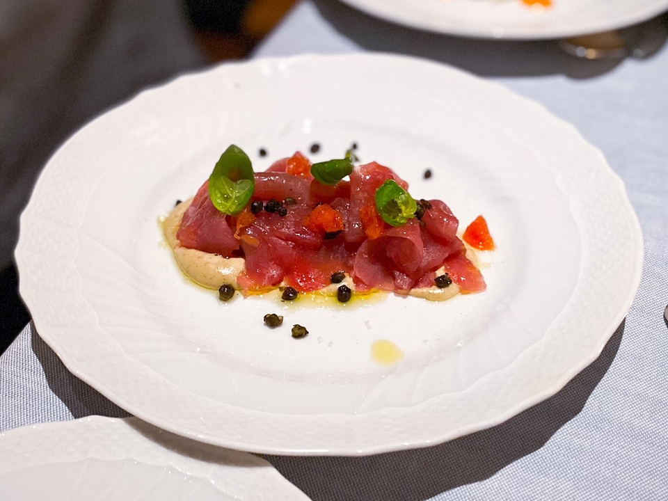 A plated dish of tuna carpaccio (tonno rosso) with diced tomatoes, capers, and basil on a white plate; the source page caption explicitly identifies t
