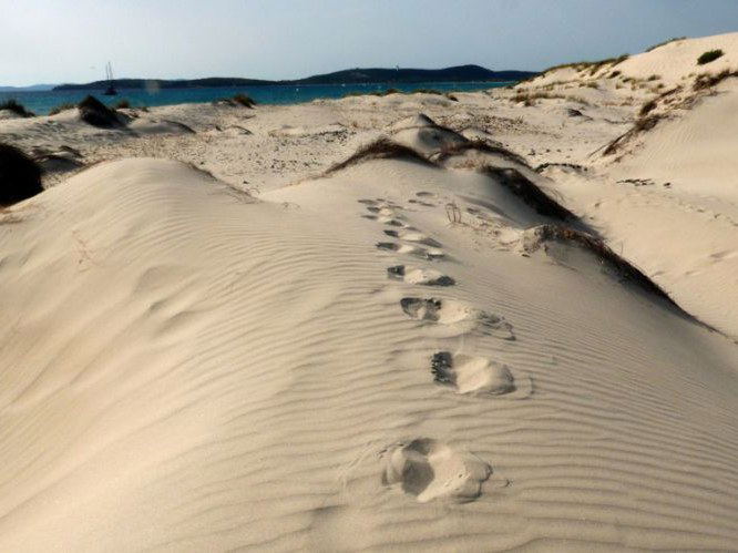 Le Dune Piscinas: footprints trace a path across golden sand dunes towards the turquoise sea.