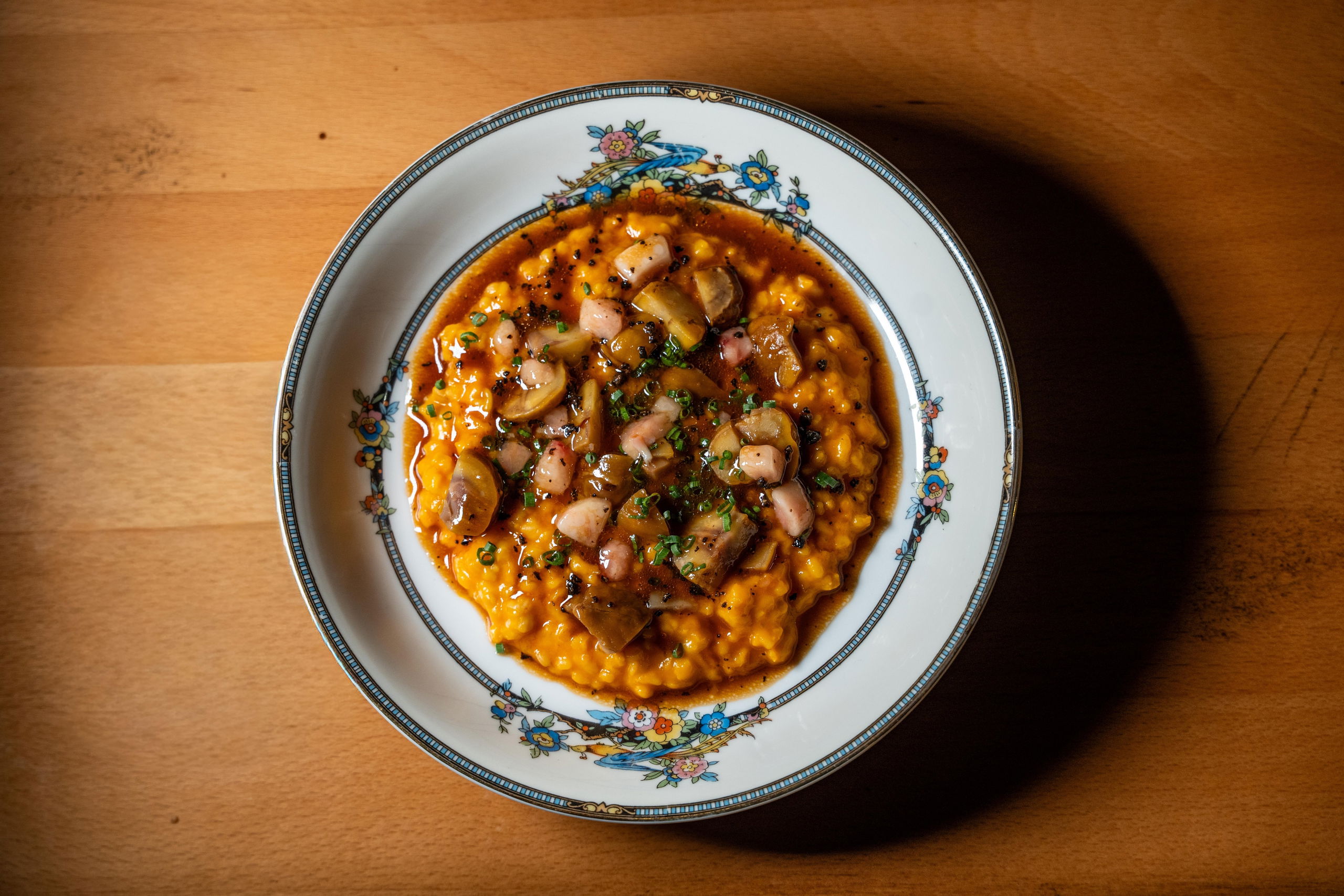A plated dish of risotto topped with sautéed mushrooms and octopus on an ornate vintage china plate, photographed from above