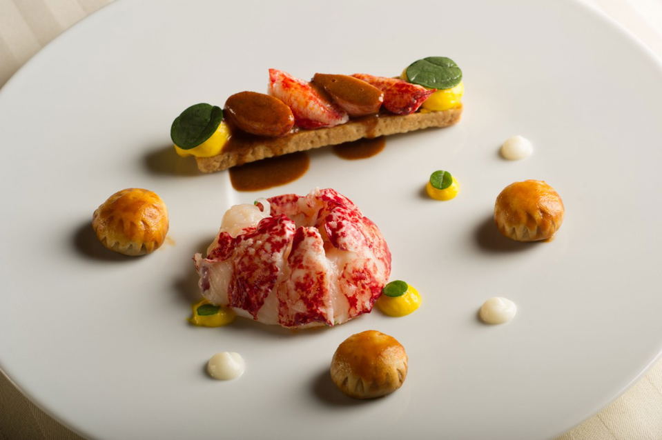 An elegantly plated fine-dining dish featuring lobster meat, crispy pastries, and colorful sauces on a white plate