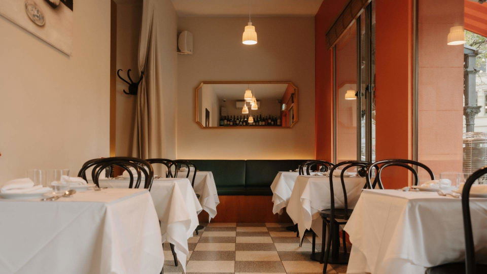 little rose fitzroy's inviting interior, featuring dark wood, backlit bottles, and bentwood bar stools.