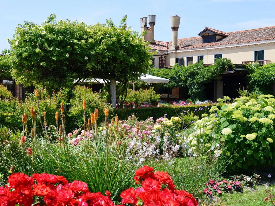 Locanda Cipriani Torcello's lush garden with vibrant flowers and a vine-covered pergola.