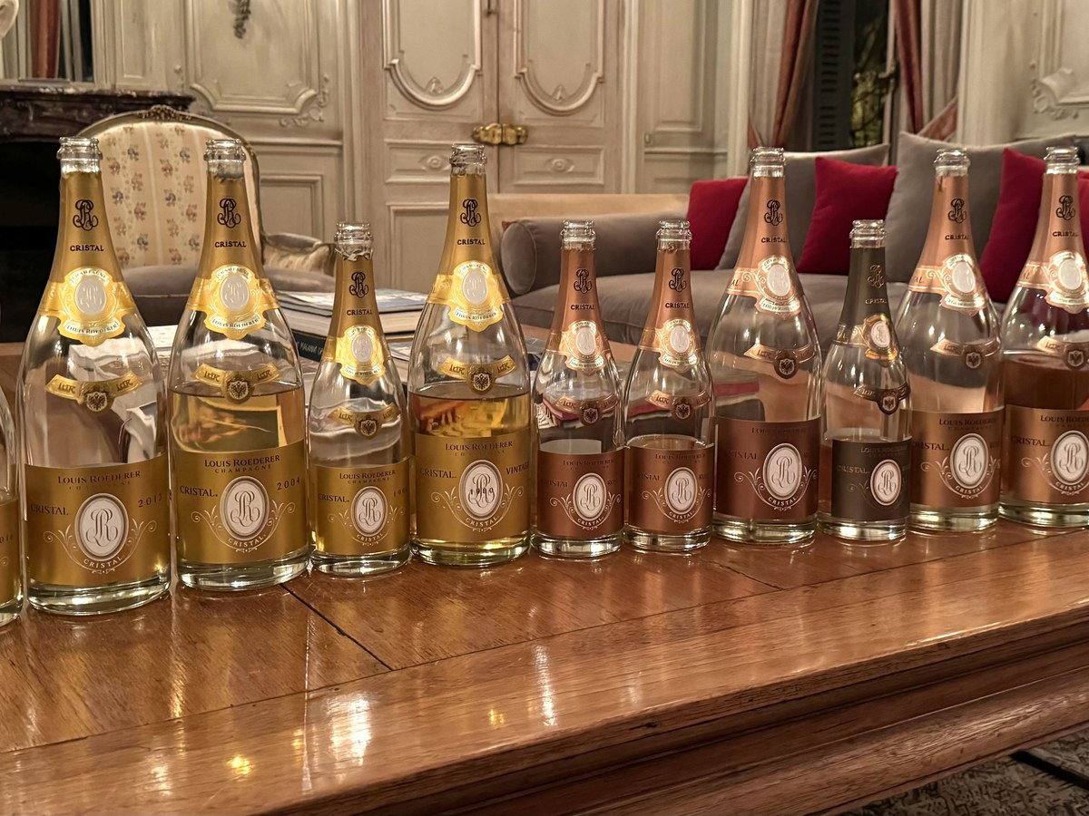 A collection of Louis Roederer Cristal and Cristal Rosé champagne bottles, some full and some empty, arranged on a polished wooden table.
