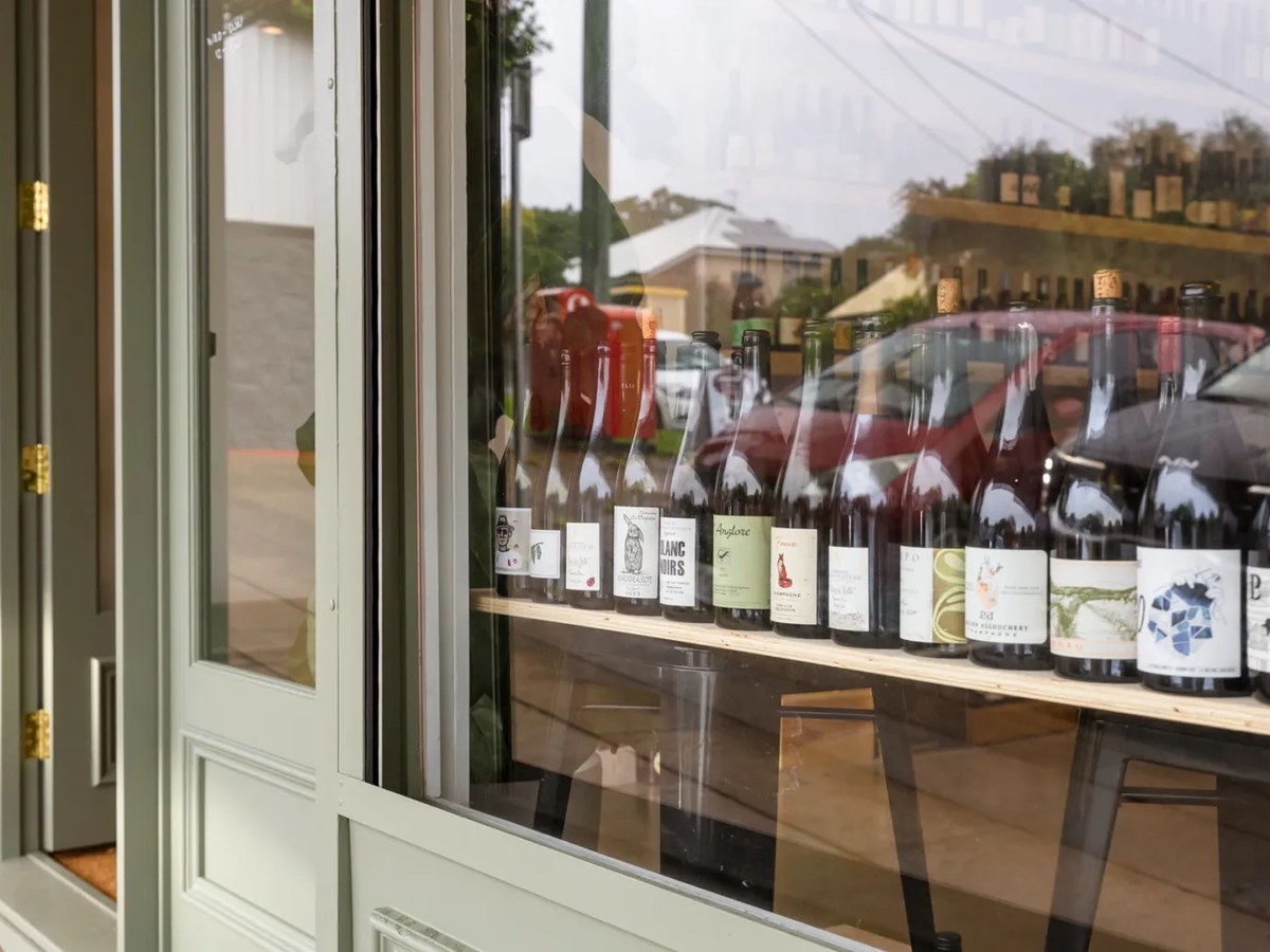 Exterior shopfront of LPO Wine Store showing a sage-green painted door and window frame with wine bottles displayed on a wooden shelf inside.