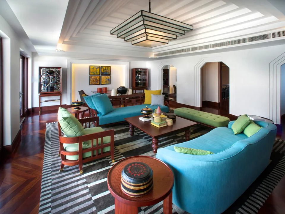 A luxurious living room at Park Hyatt Siem Reap, featuring teal sofas, green pillows, dark wood furniture, and a geometric chandelier.
