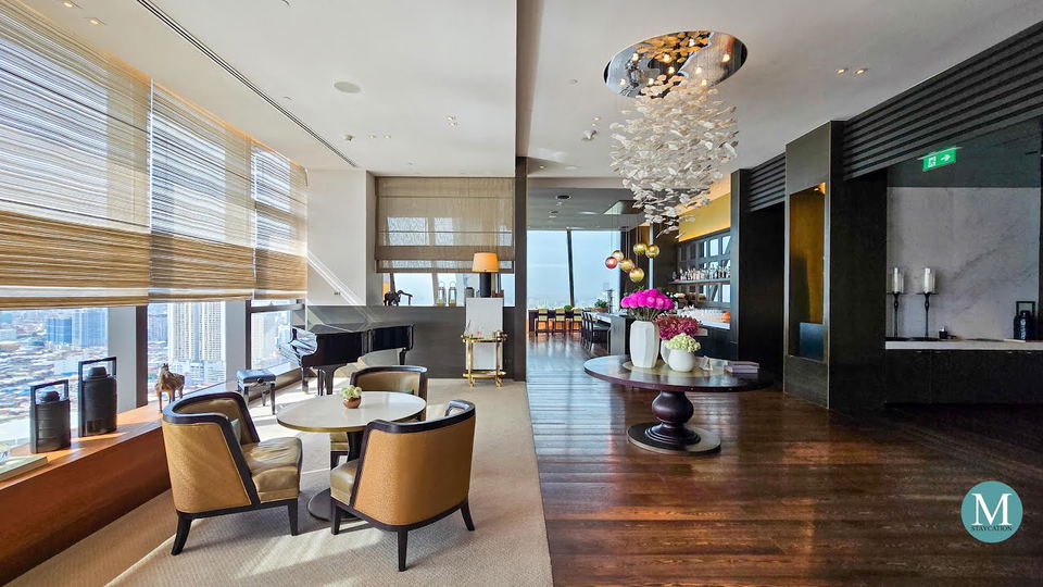 A luxurious hotel lobby with a grand piano, modern seating areas, and a bar, featuring large windows with city views and elegant decor.