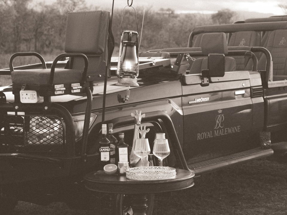 Malewane Lodge offers sundowners at dusk, with drinks and lanterns set up beside a safari vehicle.