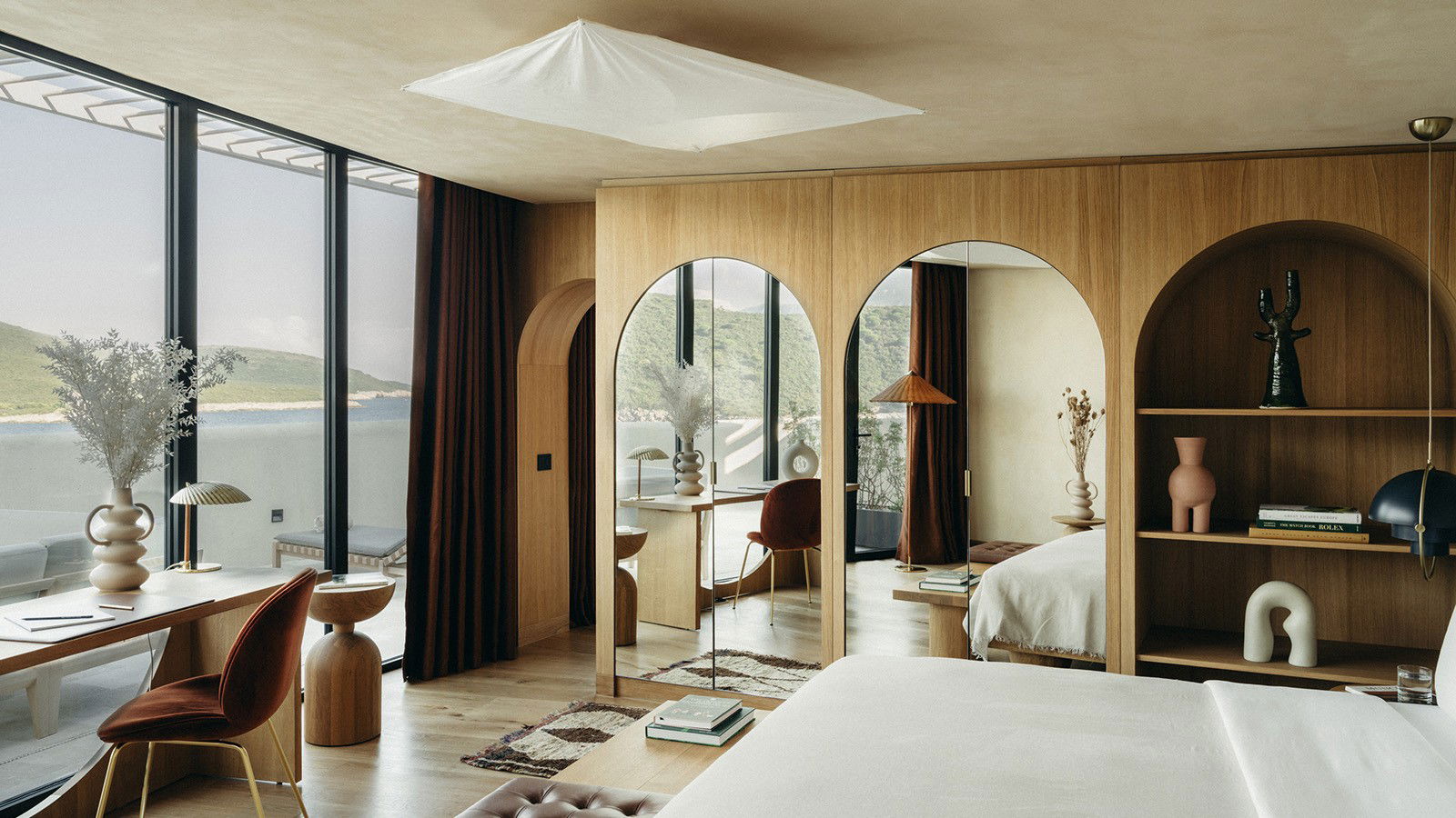 A luxury hotel suite interior with mid-century modern furnishings, arched wooden built-ins, and panoramic water views; the source page explicitly atte