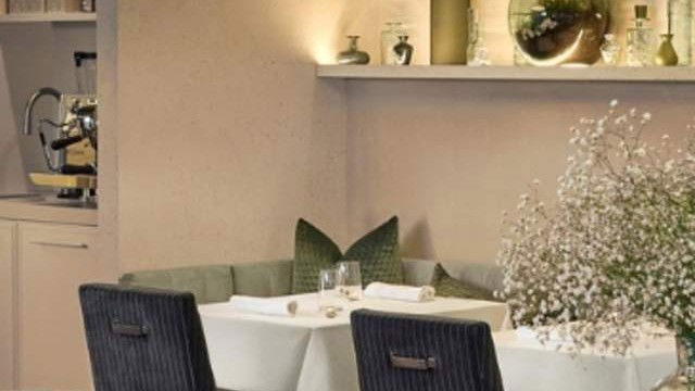 An upscale restaurant dining room interior with contemporary pendant lighting, white-clothed tables, dark wicker chairs, green accent pillows, and dec