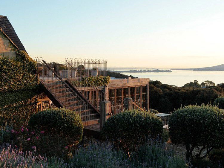 Exterior view of a wooden deck/terrace structure with stairs and decorative iron railings, surrounded by landscaped gardens with lavender and views of