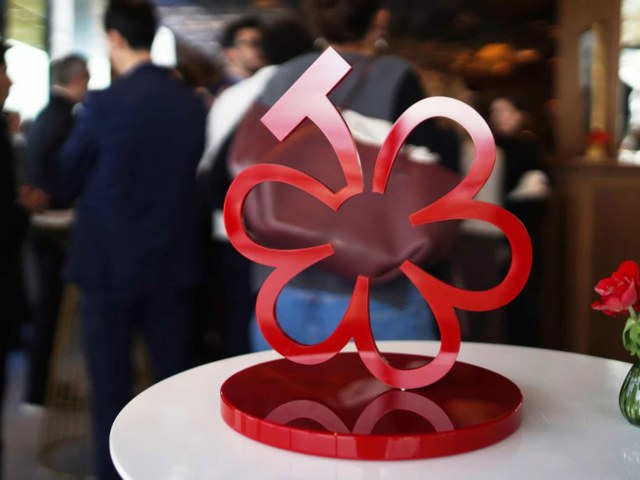A red sculptural MICHELIN Guide rating system symbol, shaped like a flower with a stem, stands on a circular base at an event.