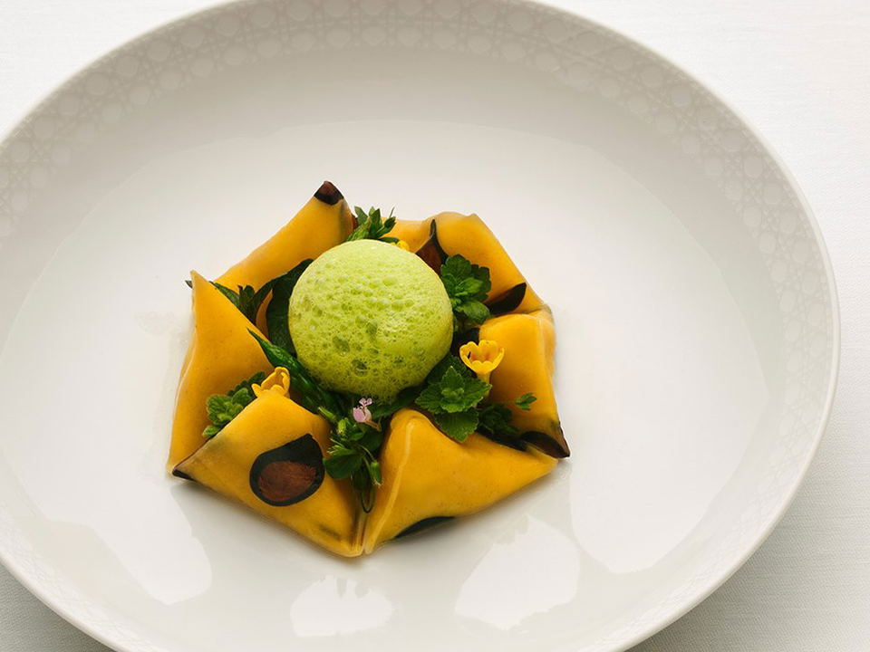 An elegantly plated fine-dining dish featuring a pale green dome (likely Le Dôme Soyeux) atop golden pasta and greens, photographed in editorial style