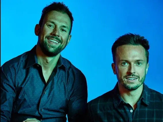 David Rekhson and Lucas Stoioff, co-founders of DineAmic Group, smile at the camera in a studio portrait against a blue background.
