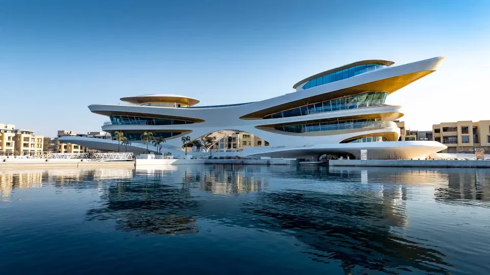 A futuristic white multi-level architectural complex with sweeping curved forms and extensive glazing sits on a waterfront marina, matching the source