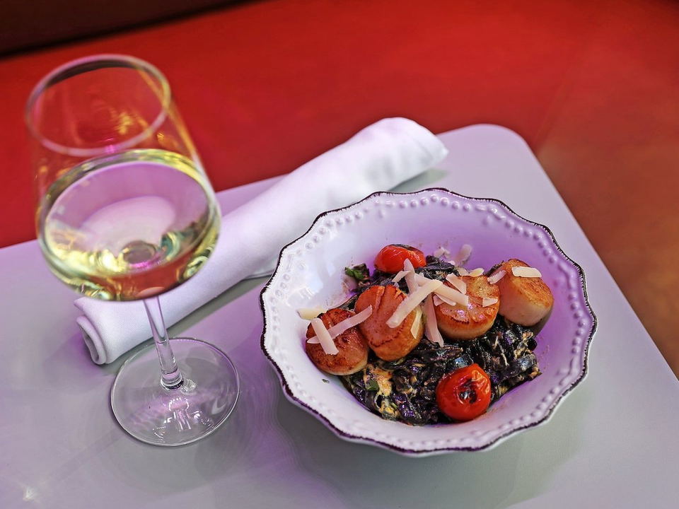Rosa y Marigold's seared scallops with dark pasta, roasted tomatoes, and shaved cheese, paired with white wine.