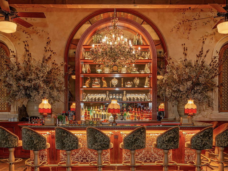 An ornate, warmly lit bar interior at Dalia's, featuring velvet bar stools, a grand arched back bar with shelved glassware and decorative objects,