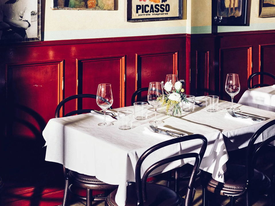 A classic French bistro dining room interior with red wainscoting, white tablecloths, bentwood chairs, wine glasses, and a "PICASSO portraits