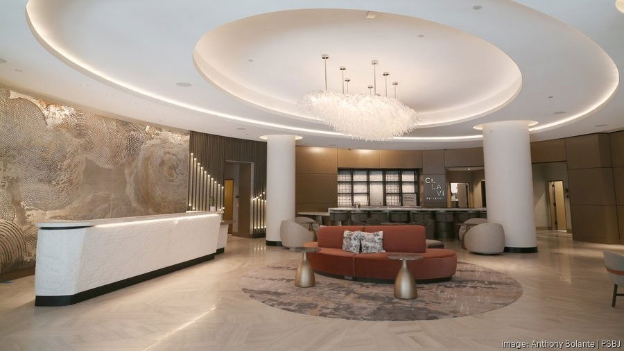 A wide interior shot of the Nobu Bellevue Residences lobby, featuring a circular coffered ceiling, a feather chandelier, and a curved terracotta sofa.