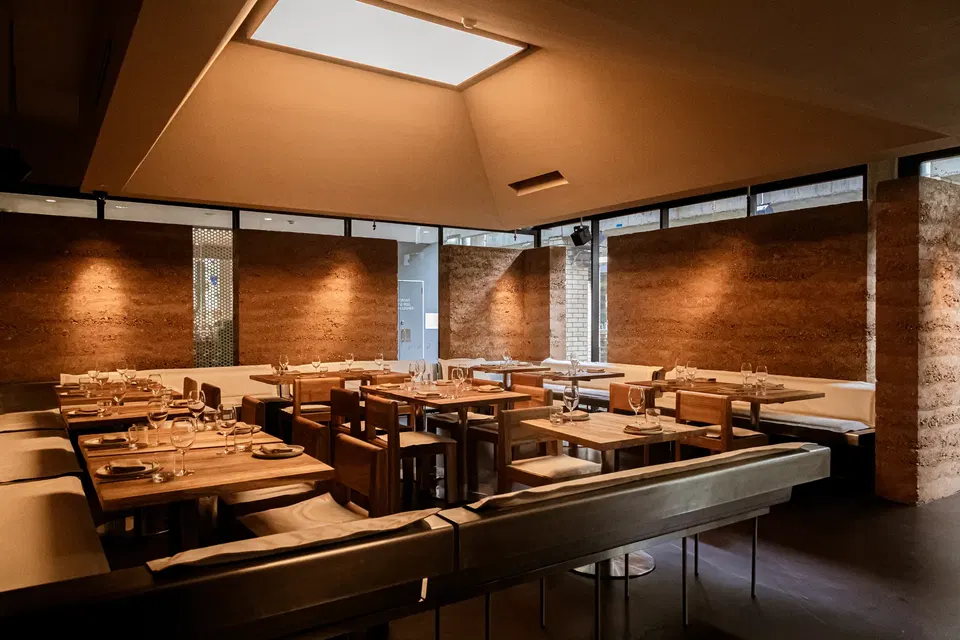 An upscale restaurant dining room with wooden tables, booth seating, textured earth-tone walls, and a skylight; the source page explicitly captions th