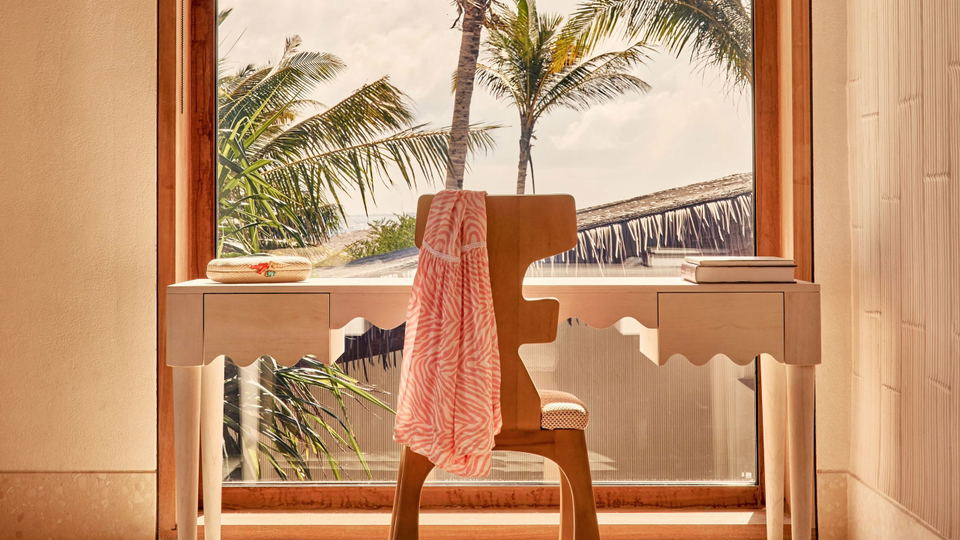 A bedroom interior with a sculptural desk, chair, and tropical view through a window