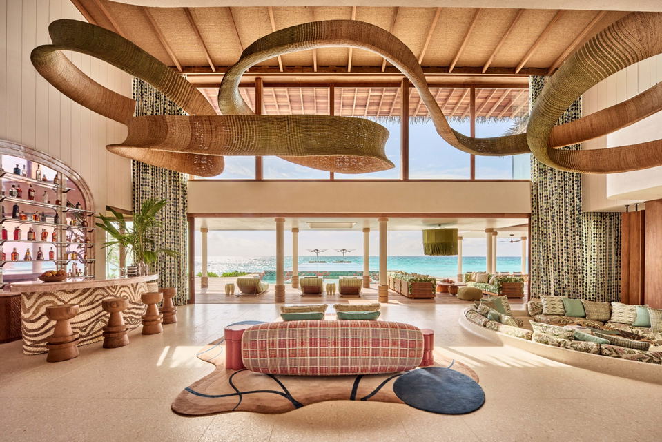 A luxury resort bar/lounge interior with sunken seating areas, large sculptural woven ceiling installation resembling coral or organic forms, ocean vi