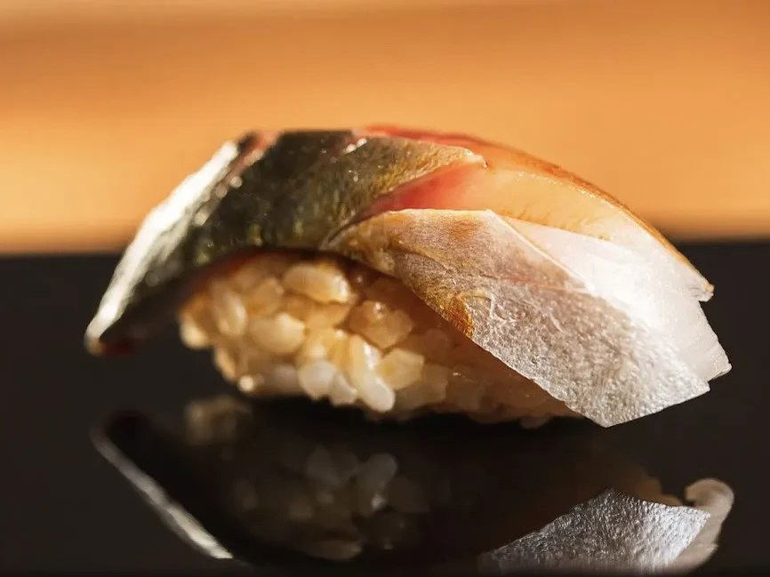 A single piece of nigiri sushi, featuring light brown rice topped with glistening fish and a dark green seaweed strip, rests on a.