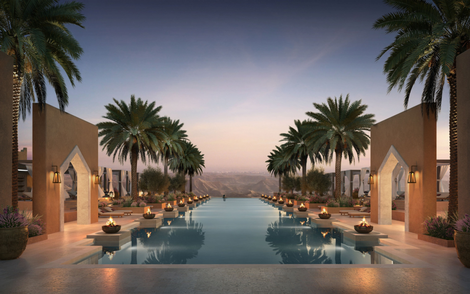 A luxury resort infinity pool at twilight flanked by palm trees, fire bowls, and contemporary Middle Eastern architecture
