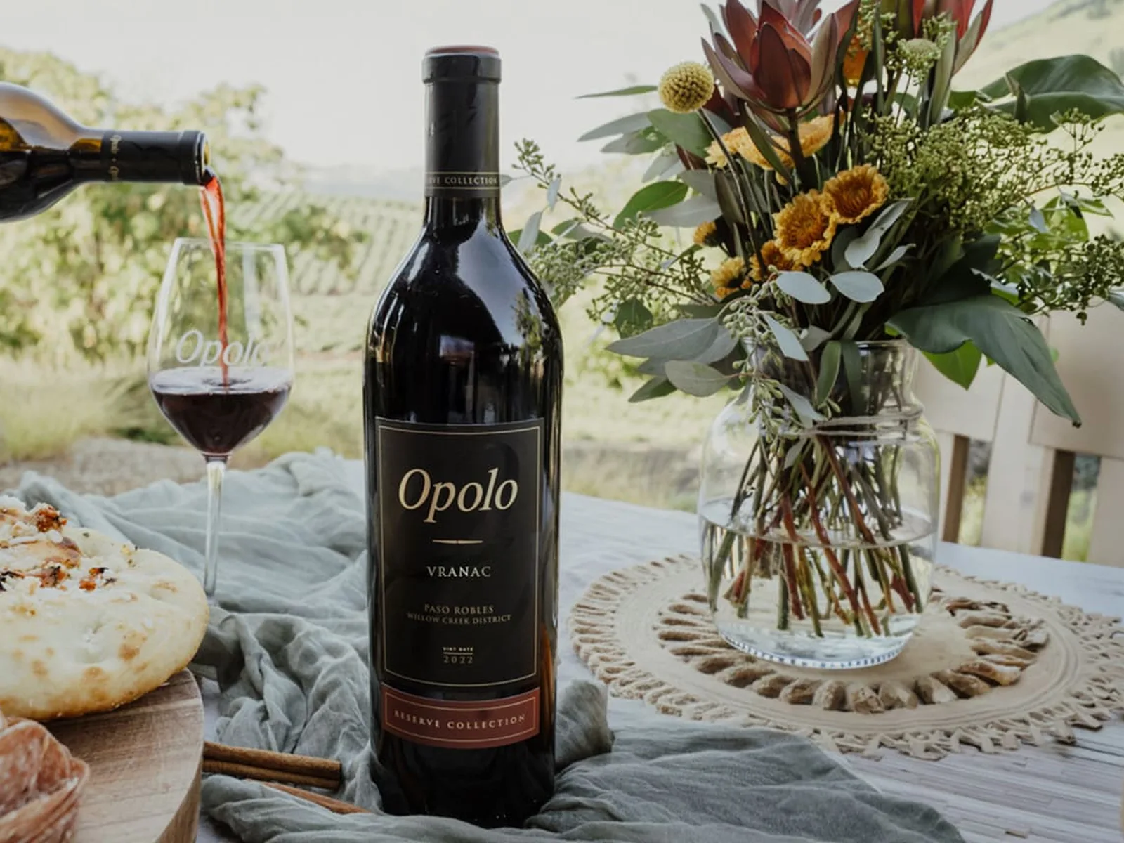 Opolo Vranac bottle, glass, flowers, food, and vineyard landscape in Paso Robles.