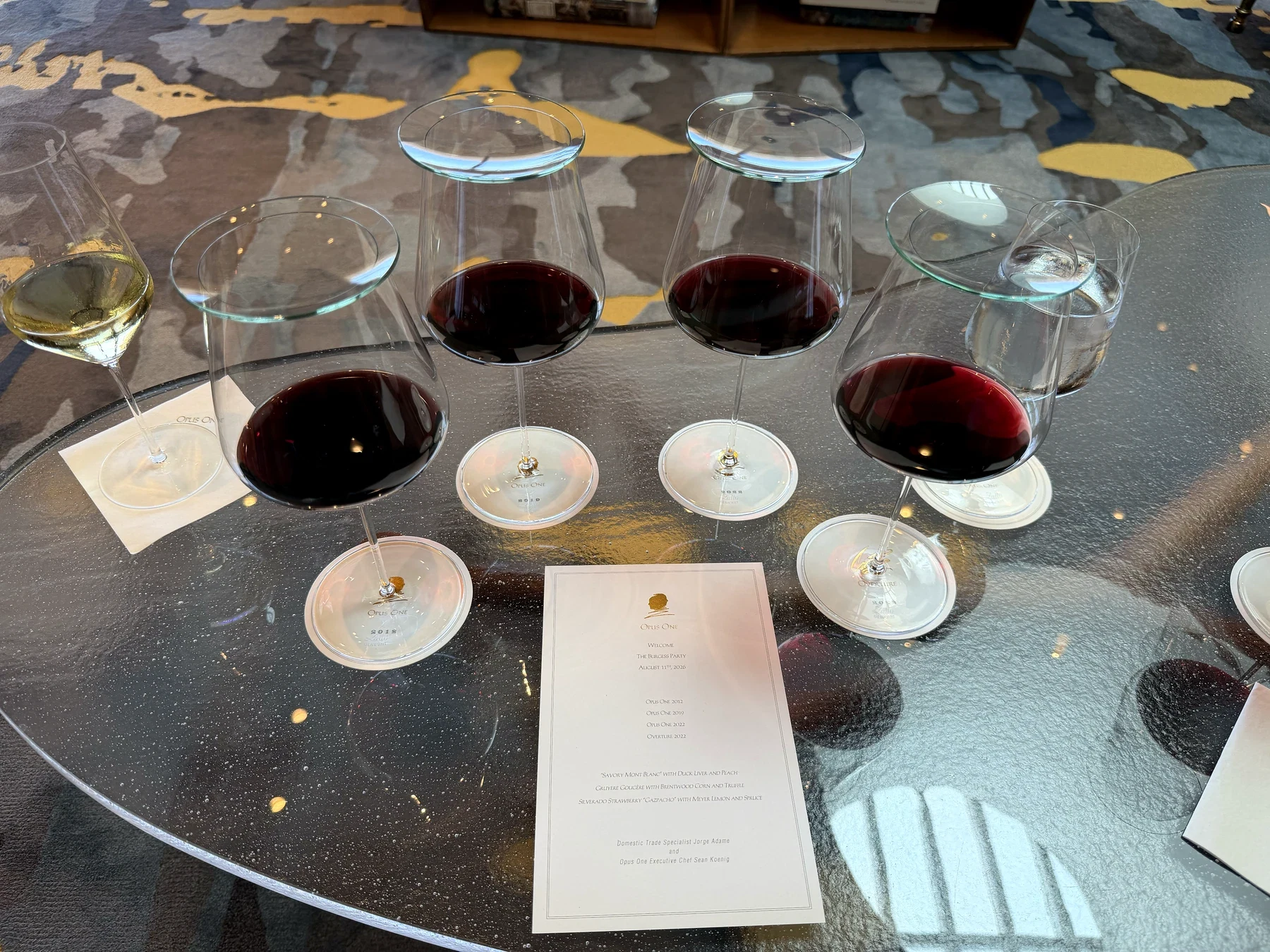 Four glasses holding Opus One 2012, 2019, 2022 and Overture 2022 around the printed tasting menu