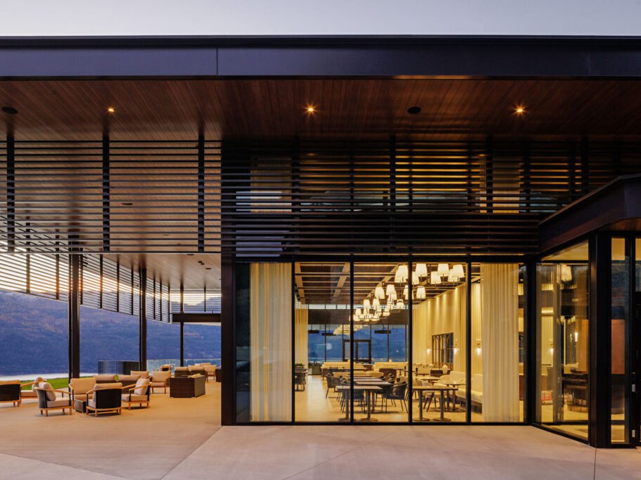 An elegant modern dining room with pendant chandeliers and tables set for evening service, seen from an exterior terrace at dusk.