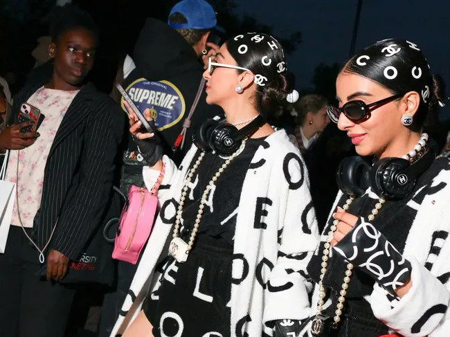 Paris Fashion Week street style: Attendees in bold Chanel-branded outfits with headphones and bags, photographed in a crowd.