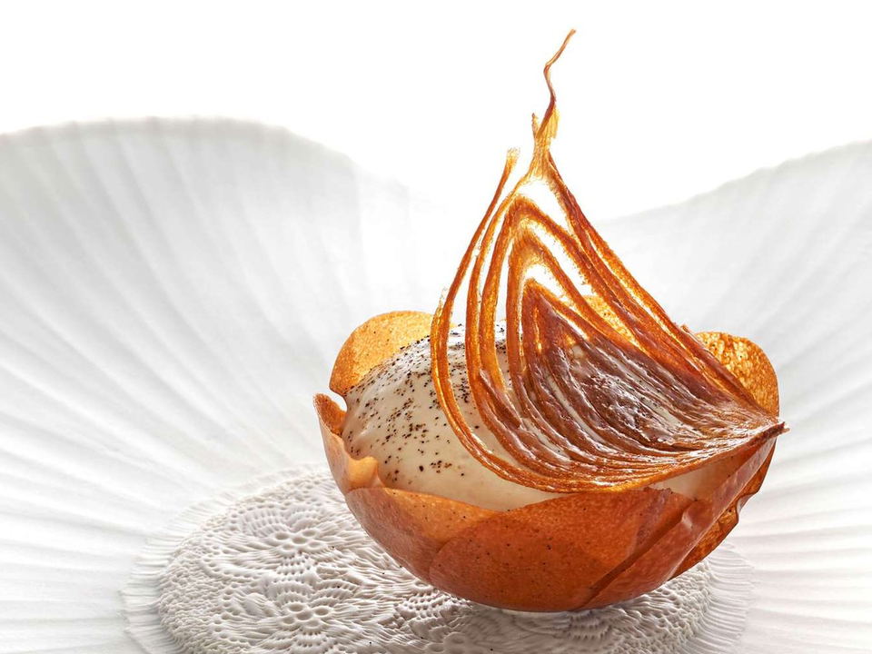 A highly artistic plated dessert in a caramelized tuile basket with a dramatic spun-sugar or pulled-caramel sail garnish and vanilla cream filling.