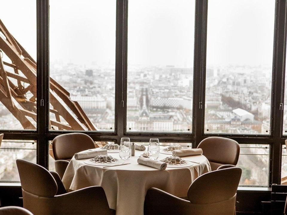 An elegantly set round dining table for four at Jules Verne restaurant inside the Eiffel Tower, with a view of Paris.