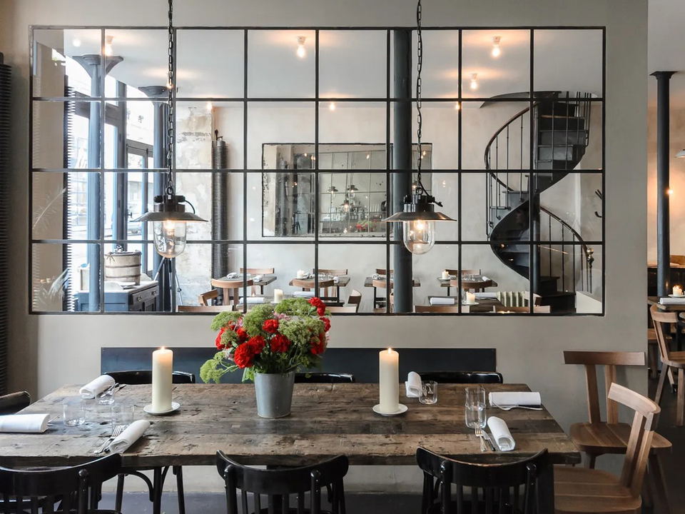 The interior of Septime restaurant in Paris, featuring a long communal wooden table with candles and a floral centerpiece, and smaller tables.