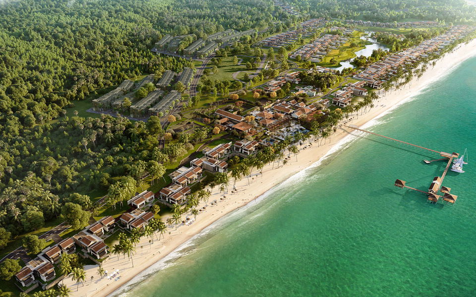 Aerial view of a beachfront resort development showing village-style architecture with courtyards, pathways, gardens, and villas leading to turquoise 