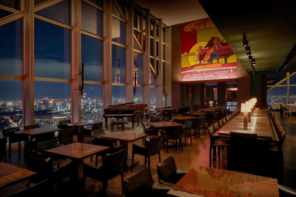 The New York Bar at Park Hyatt Tokyo, with the Valerio Adami mural, live-jazz stage, and Tokyo skyline at night.
