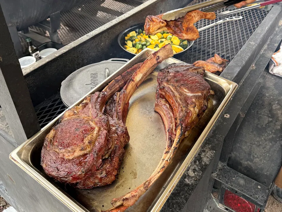 Tomahawk steaks and chicken beside an outdoor smoker at Paws Up