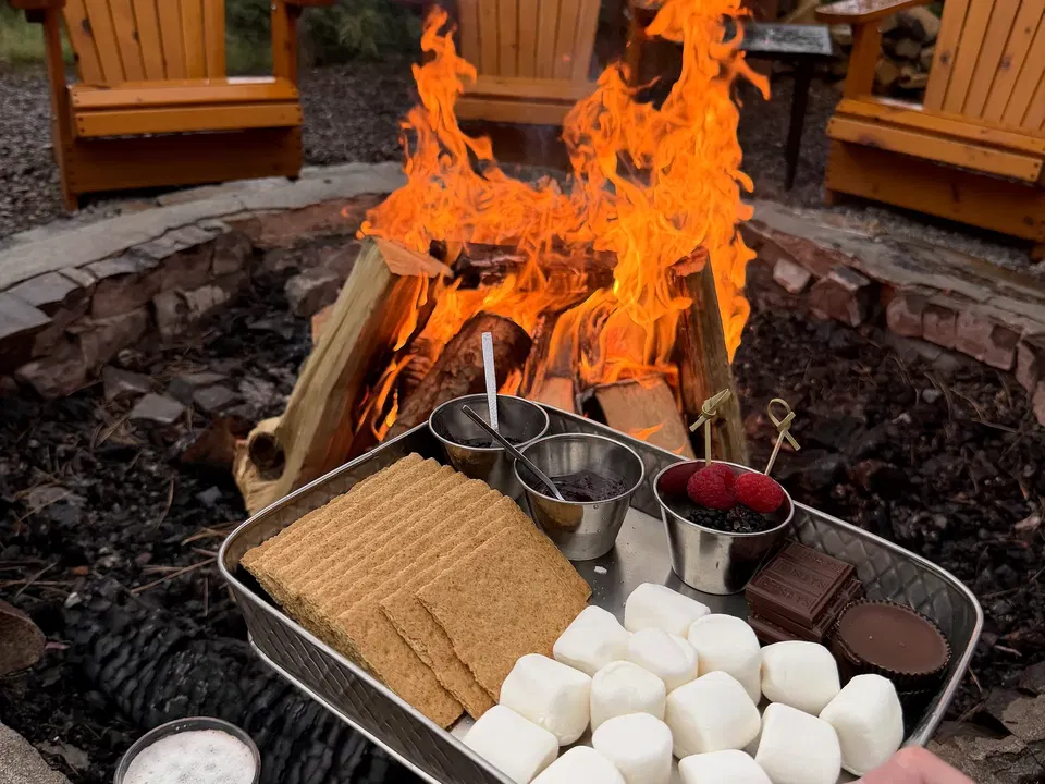 Tray of marshmallows, graham crackers, chocolate, and berries beside a Paws Up campfire