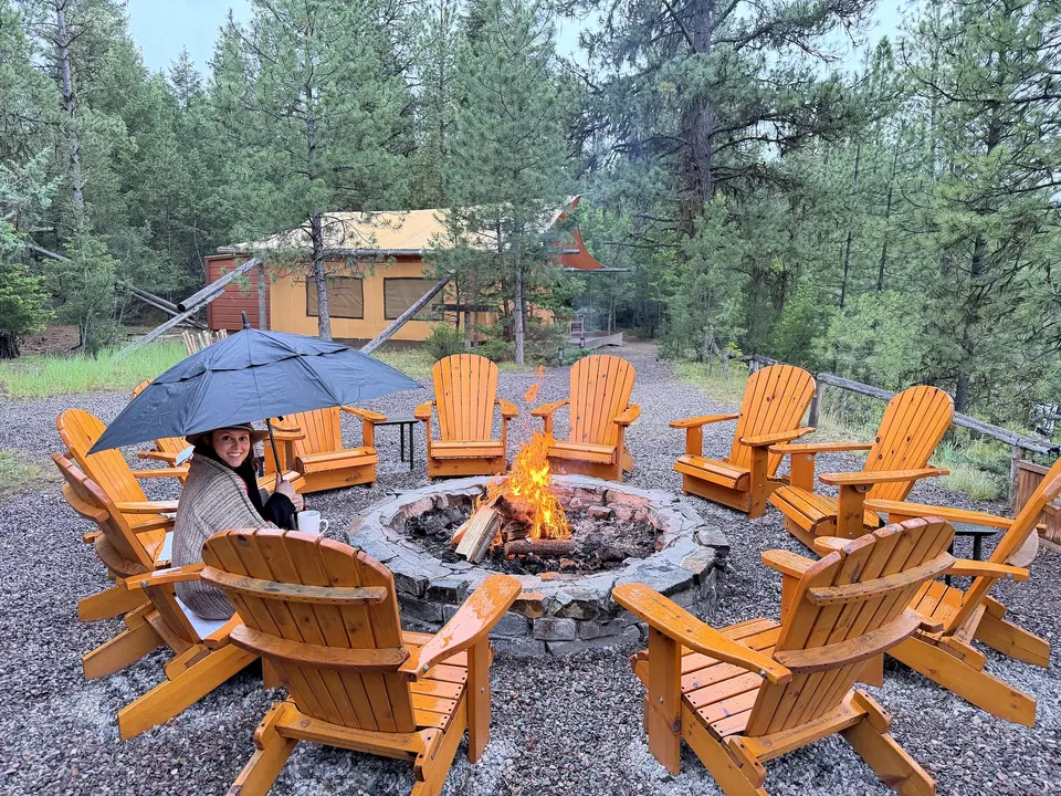 Guest holding an umbrella beside a campfire at rainy Cliffside Camp