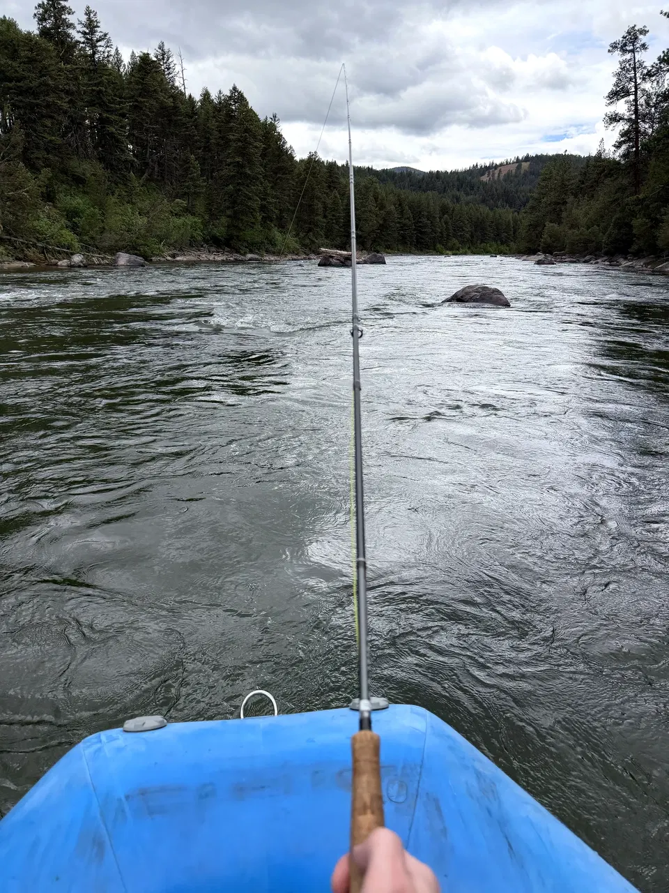 Fly rod pointing down the Blackfoot River from a blue fishing raft