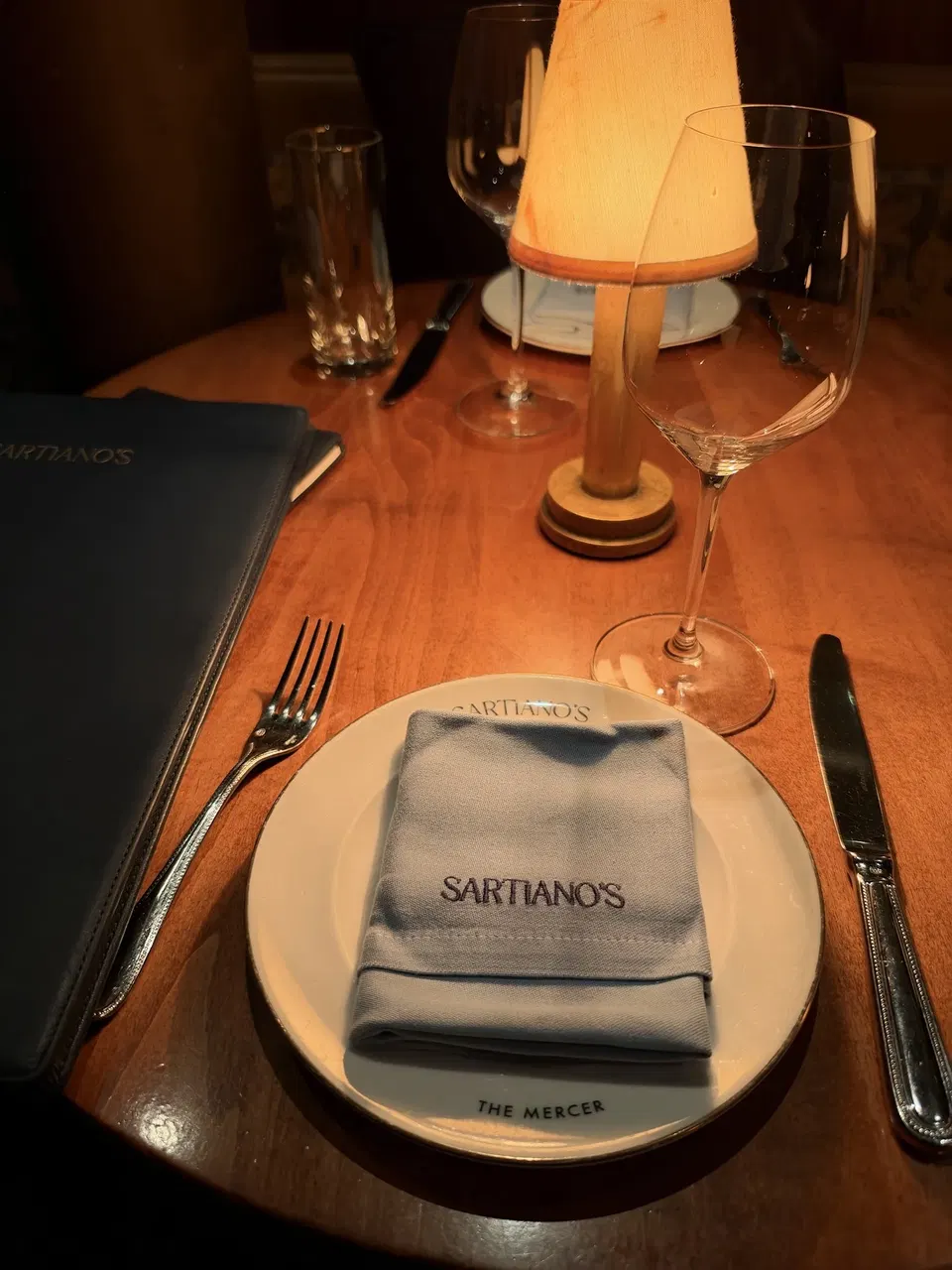 A shaded table lamp and Sartiano’s place setting.
