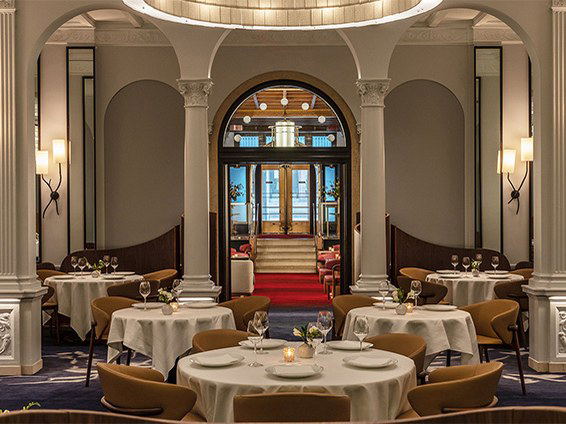 An elegant dining room at Daniel restaurant on the Upper East Side, with white-tableclothed round tables, ornate columns, and wall sconces.
