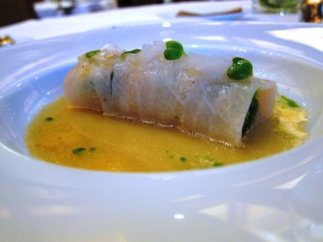 Fish roll in broth with green sauce on a white plate.